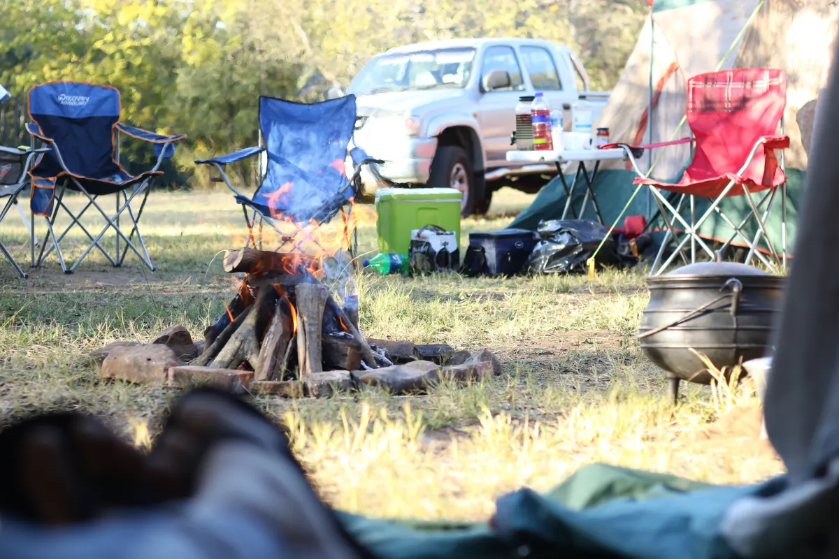 Camp chairs and a cooking fire among tents at a busy campsite