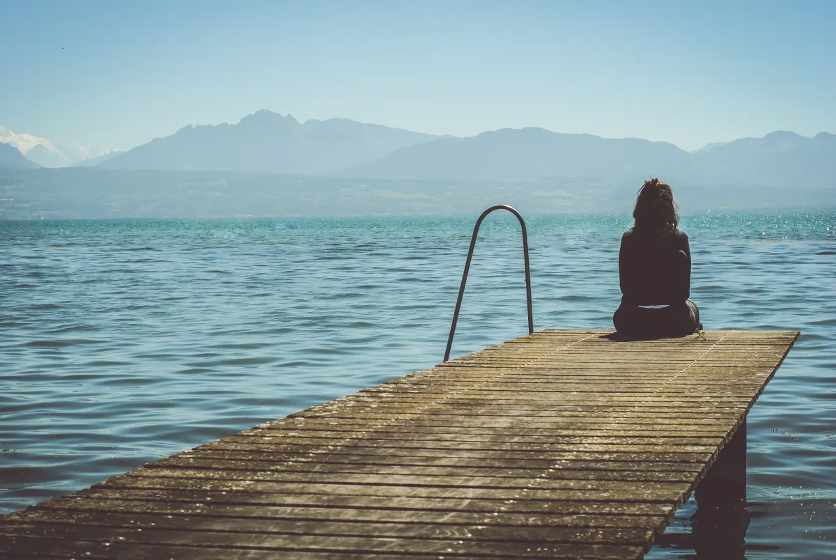 A person sitting at the end of a wooden dock over a calm lake