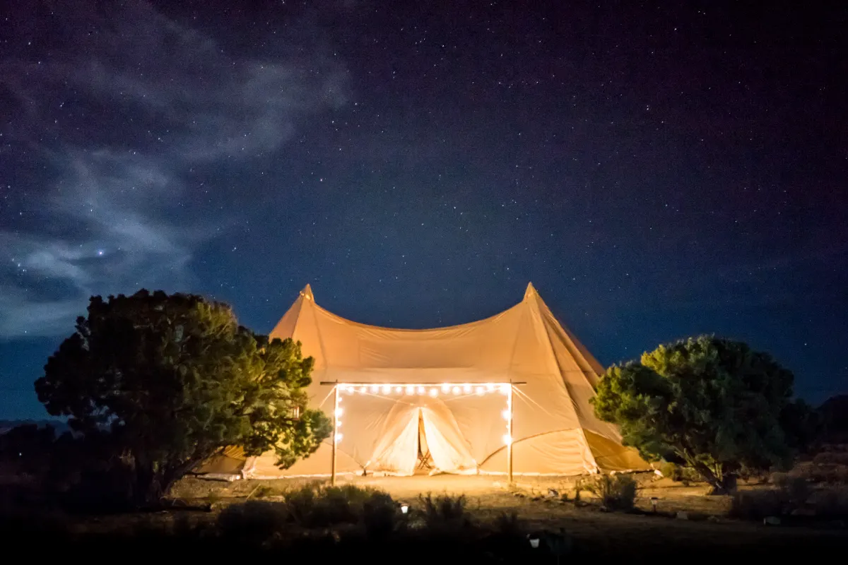 A glowing canvas glamping tent lit from inside under a starry sky