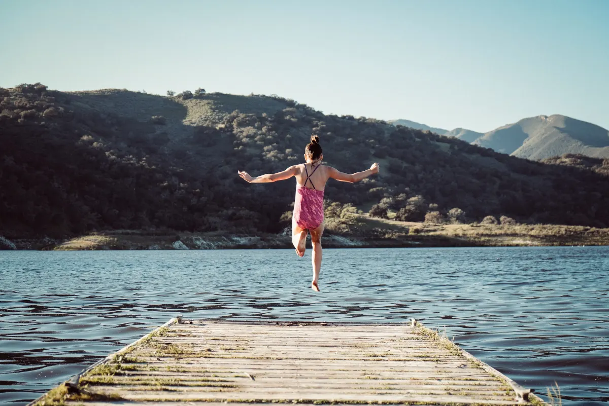 A swimmer mid-air jumping from a wooden dock into a lake